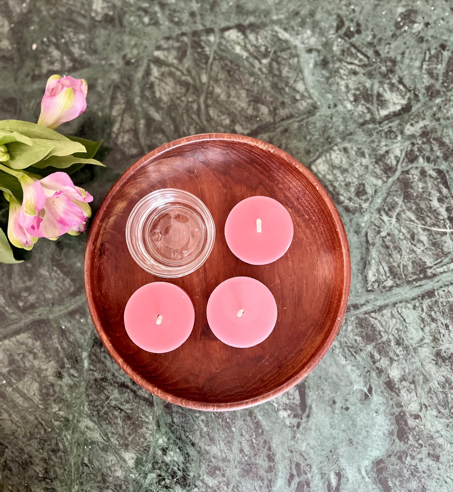 Tre telys av ren bivoks i fargen rosé og en telysholder som ligger utstilt på et bord.