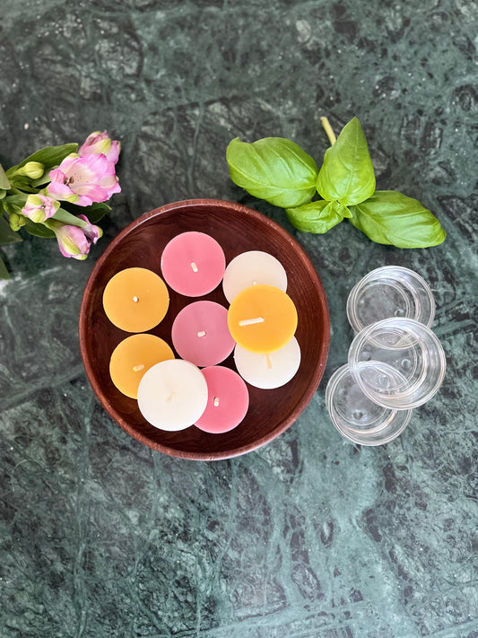 Mange telys av ren bivoks i tre ulike farger som ligger i en skål av tre på en marmorplate.