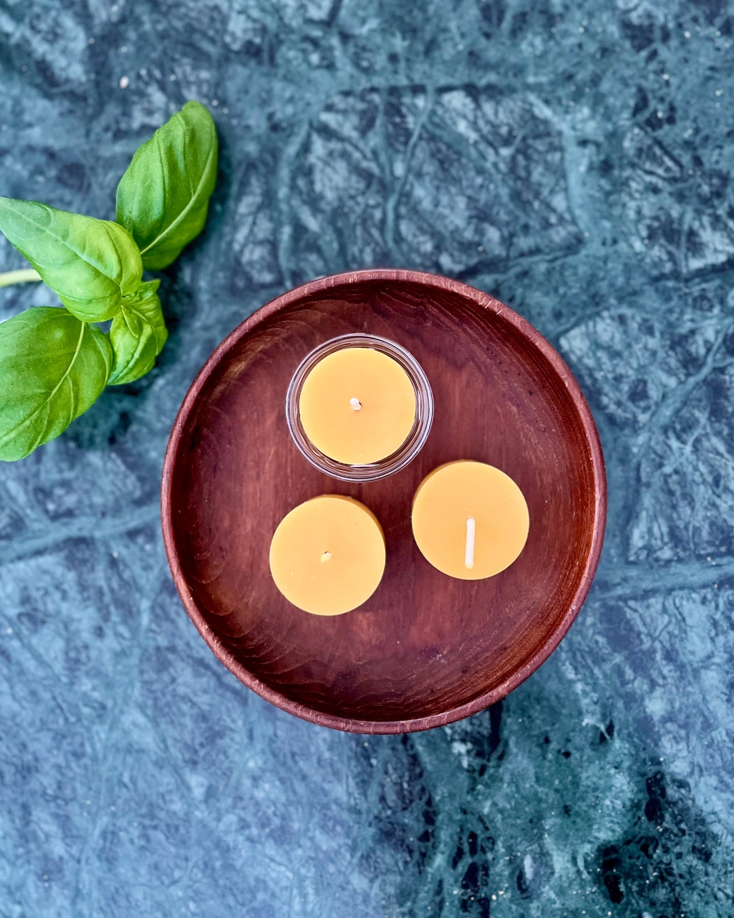 Tre telys av ren bivoks i fargen honning og en telysholder som ligger utstilt på et bord. 