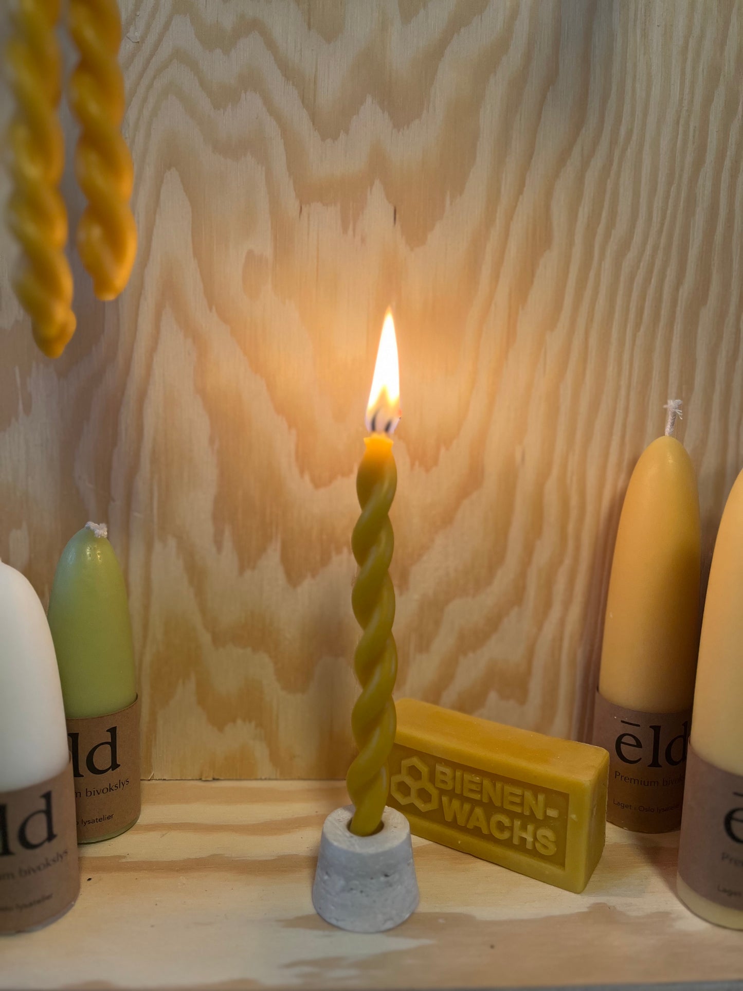 To bivokslys som er tvinnet sammen til et vakkert festlys. Lyset står utstilt på et trebord. 