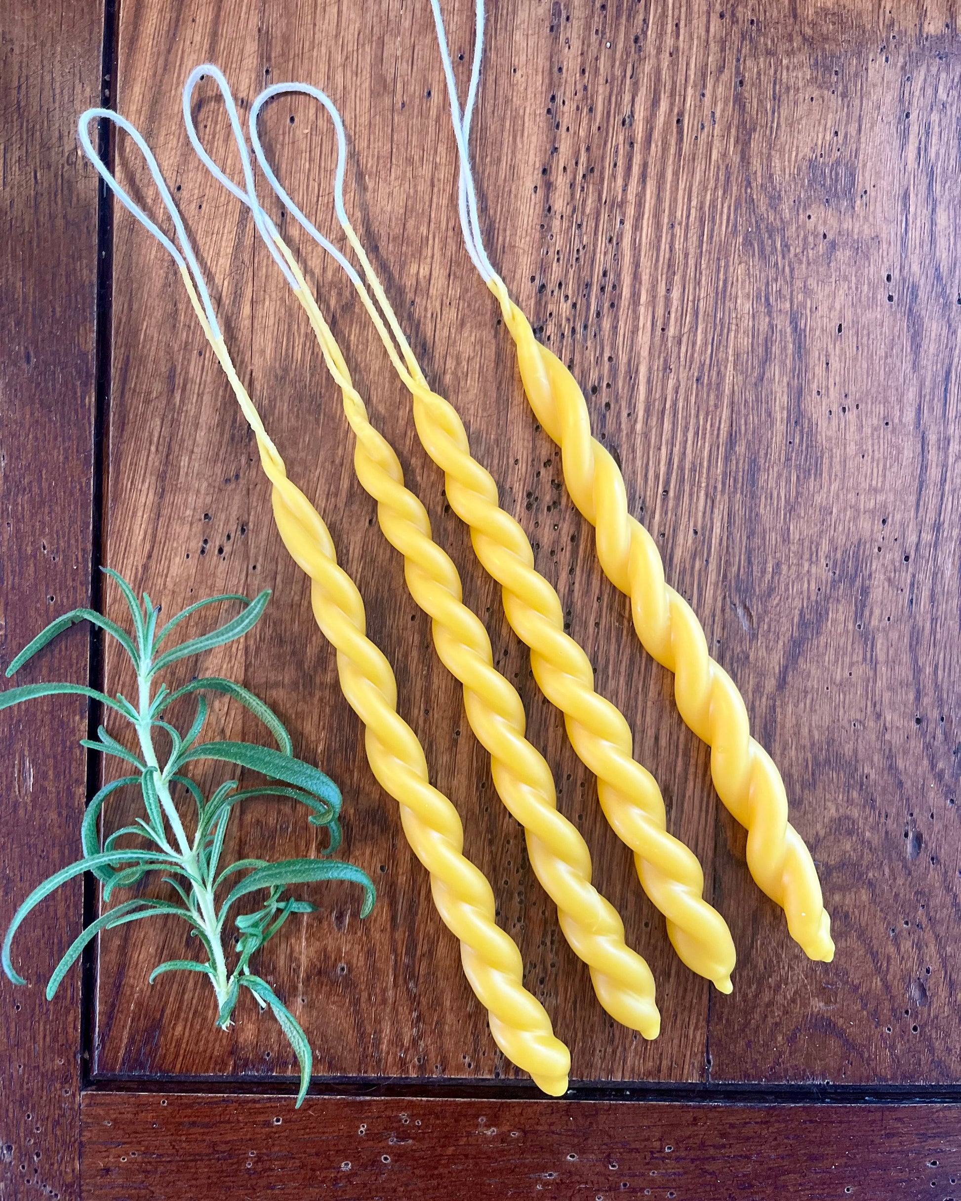 To bivokslys som er tvinnet sammen til et vakkert festlys. Lysene ligger utstilt på et trebord. 