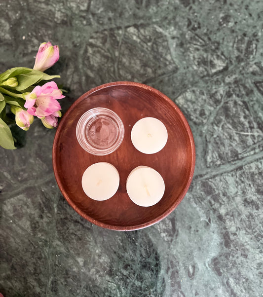 Tre telys av ren bivoks i fargen naturhvit og en telysholder som ligger utstilt på et bord. 