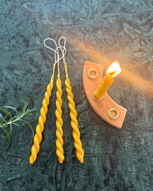 To bivokslys som er tvinnet sammen til et vakkert festlys. Lysene ligger utstilt på en marmorplate. 