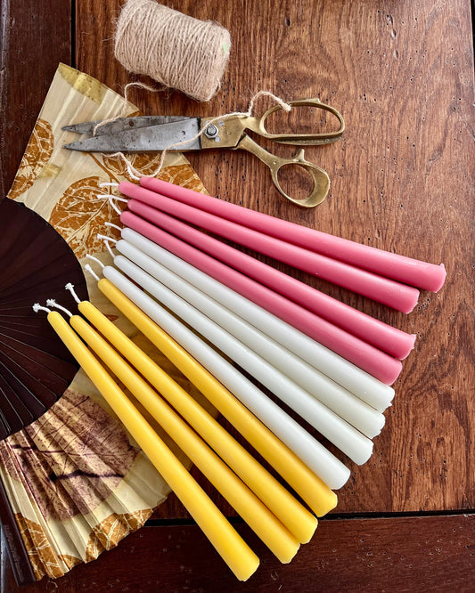 Bivoks kronelys i fargene honning, naturhvit og rose som ligger sammen på et bord. 